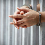 Hands in handcuffs behind prison bars