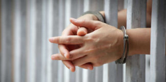 Hands in handcuffs behind prison bars