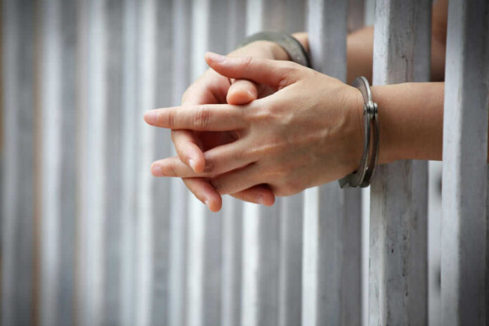 1031018551 Hands in handcuffs behind prison bars