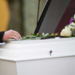 Hand resting on coffin adorned with flowers
