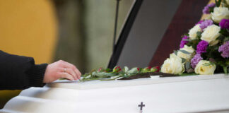 Hand resting on coffin adorned with flowers