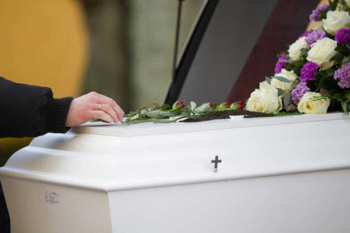 shutterstock_1614173725 Hand resting on coffin adorned with flowers